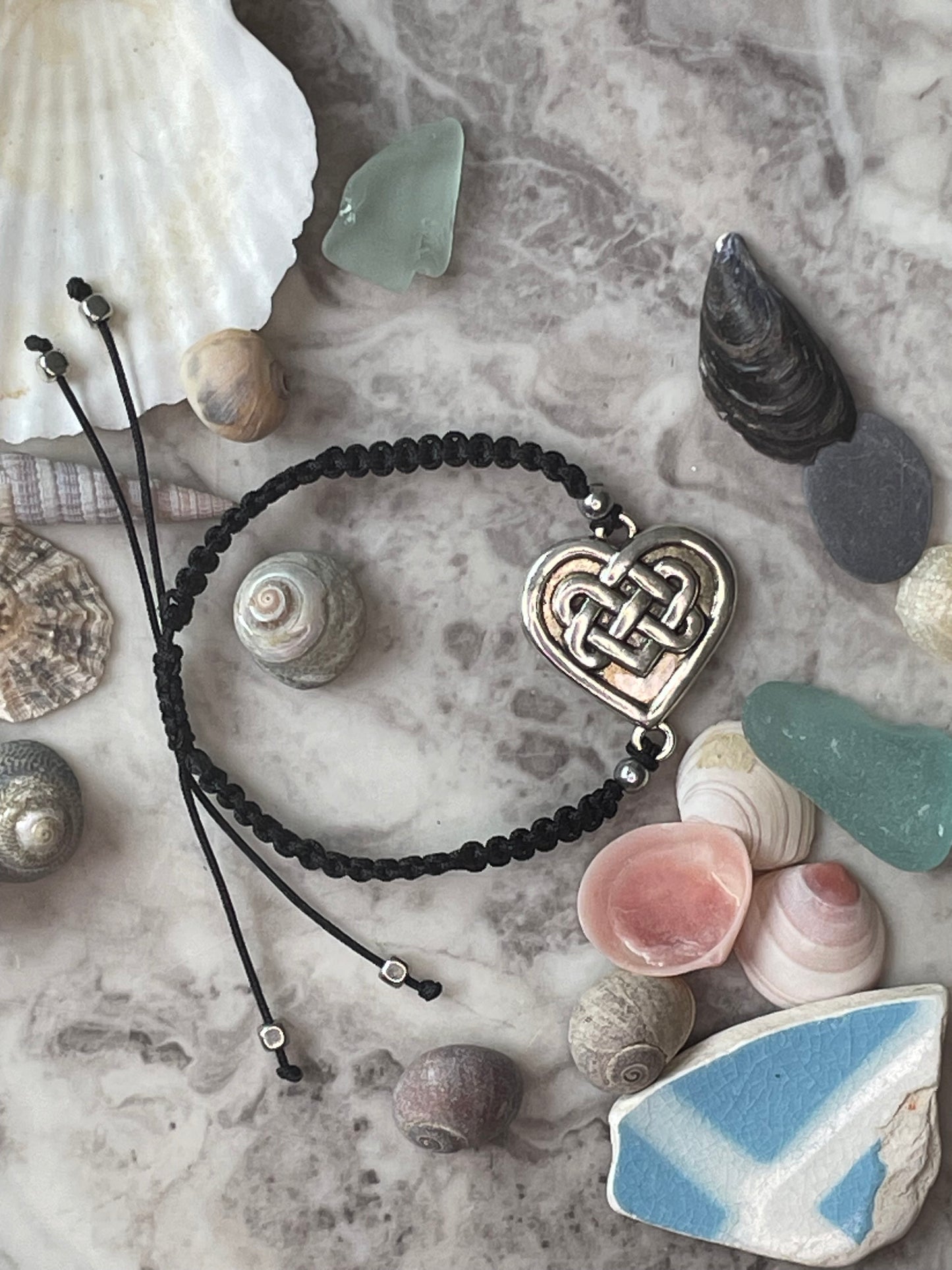 Celtic heart charm on macrame bracelet band with bead stoppers with seashells in background