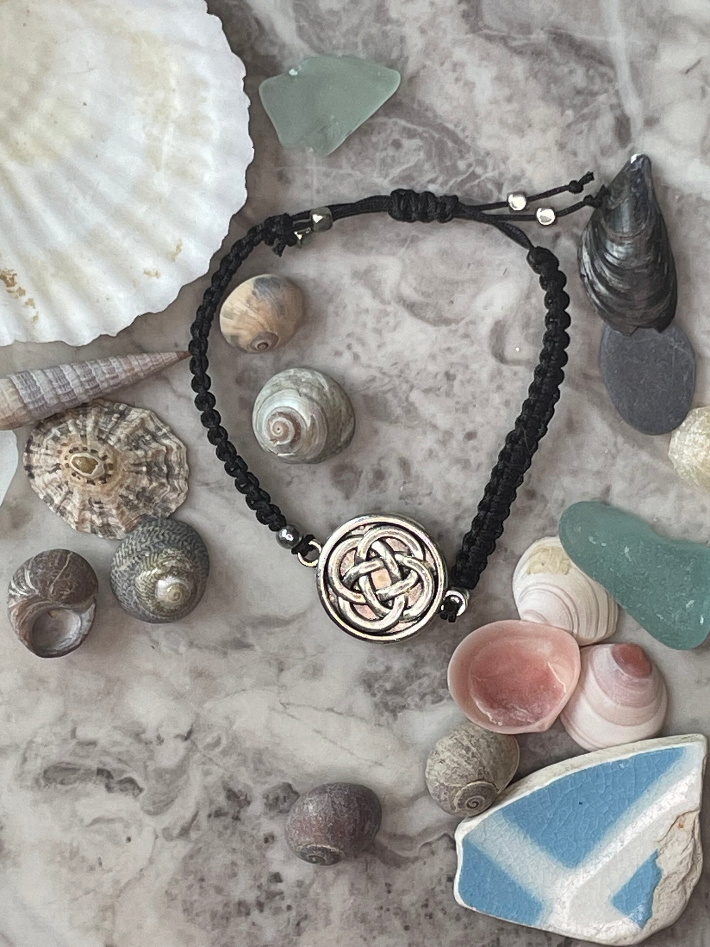 Celtic knot charm on macrame bracelet band with bead stoppers with seashells in background