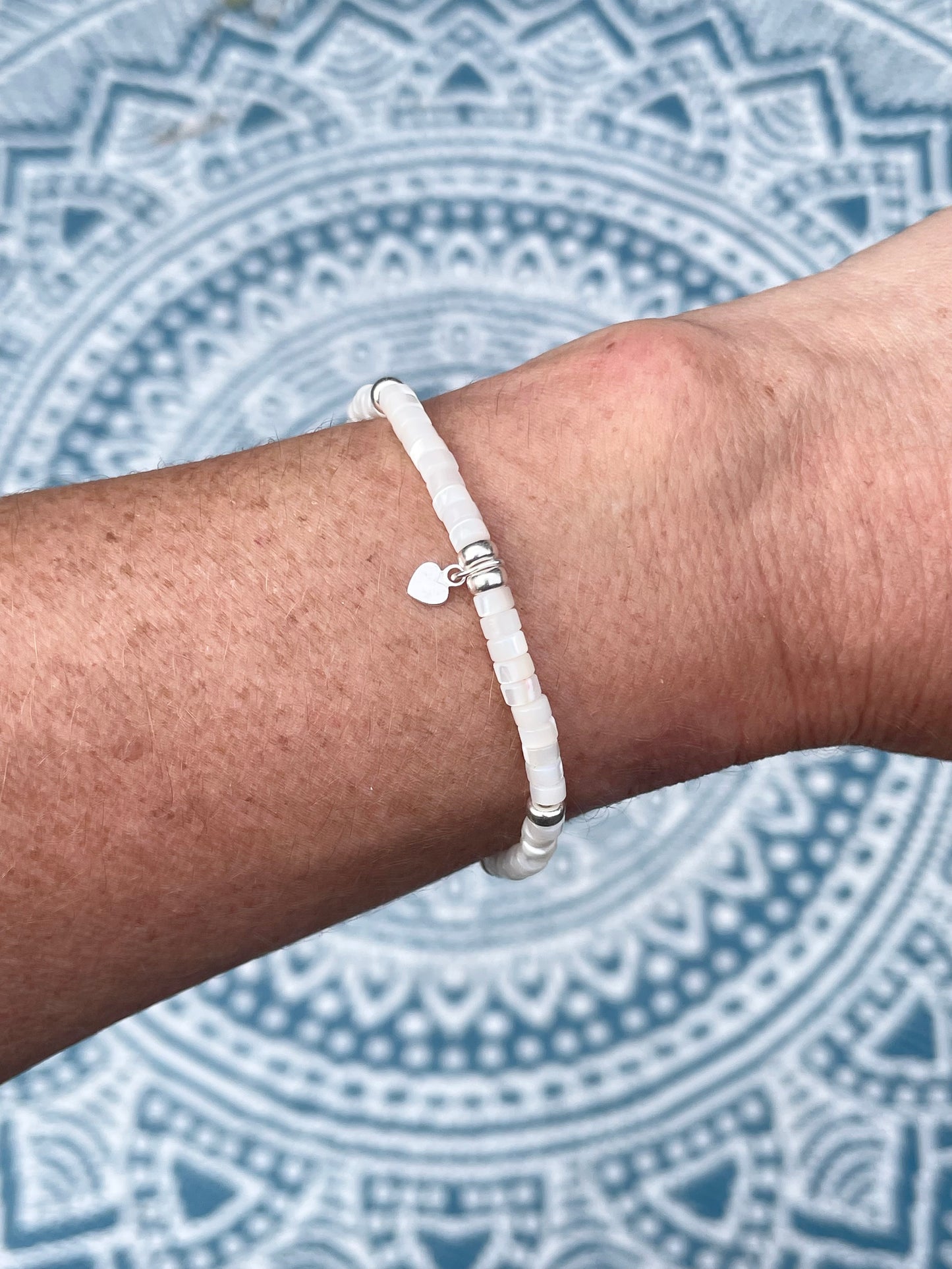 Mother of pearl heishi bead with sterling silver charm bracelet worn on wrist with mandala background