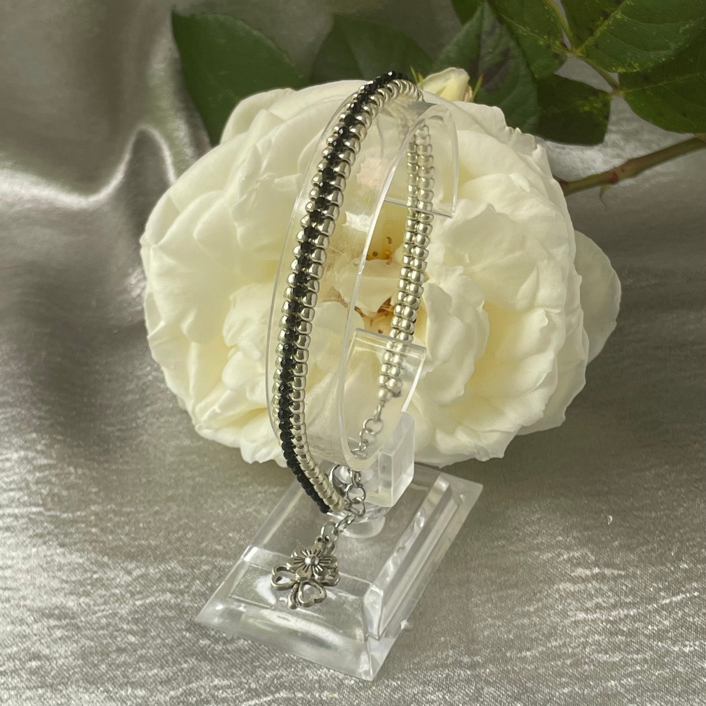 Seed bead and crystal bracelet on clear stand with white rose in background