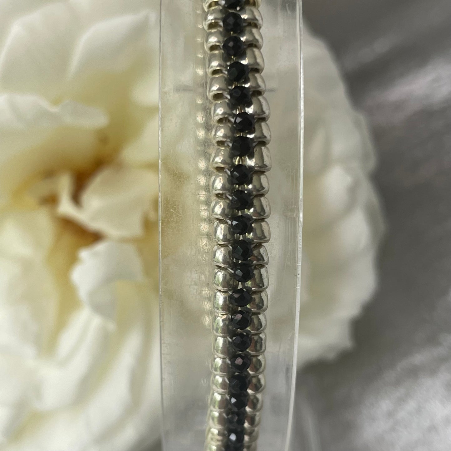 Close up of seed bead and crystal bracelet on clear stand  with white rose in background