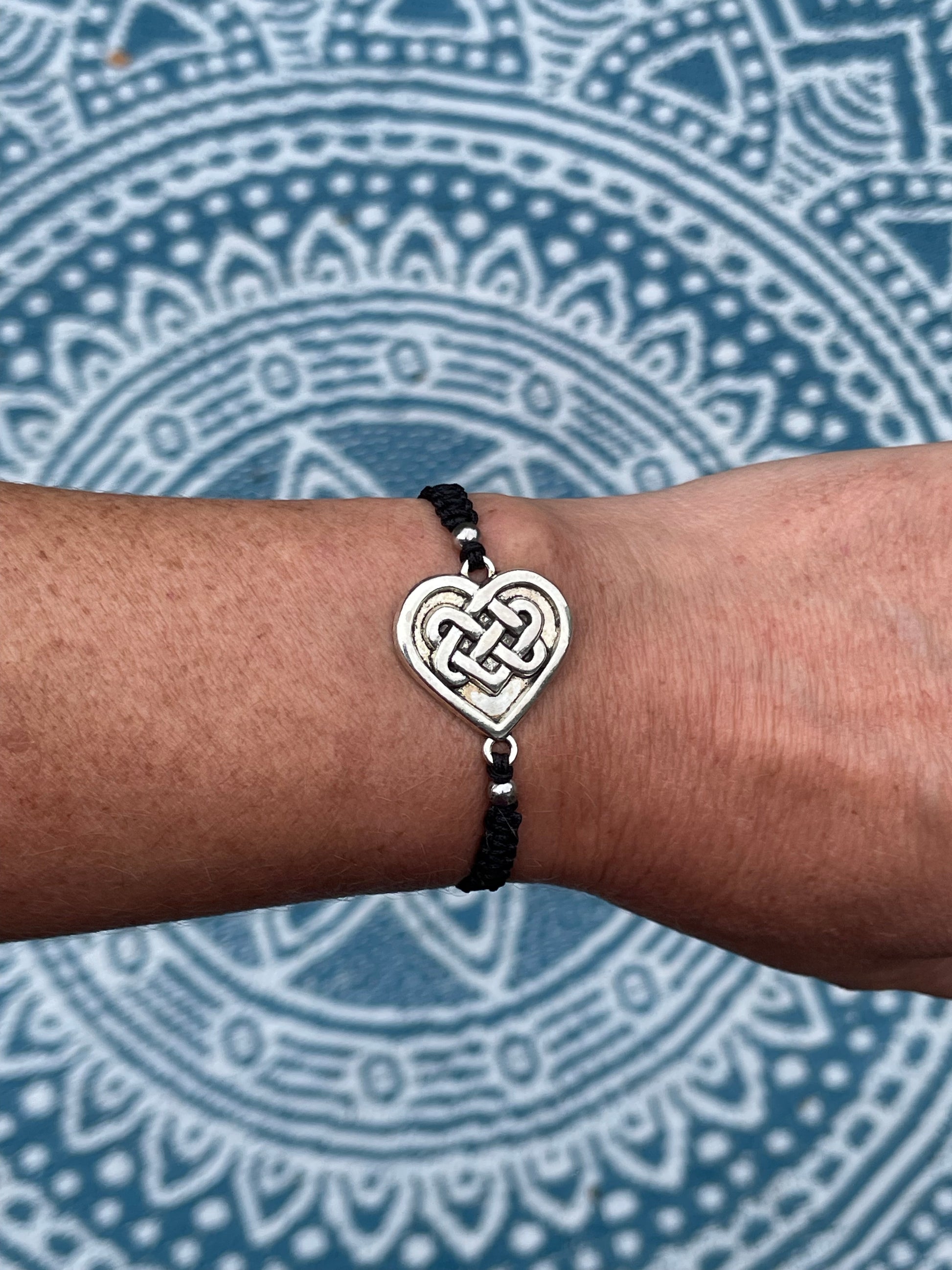 Celtic heart charm on macrame bracelet band with bead stoppers on wrist with mandala background