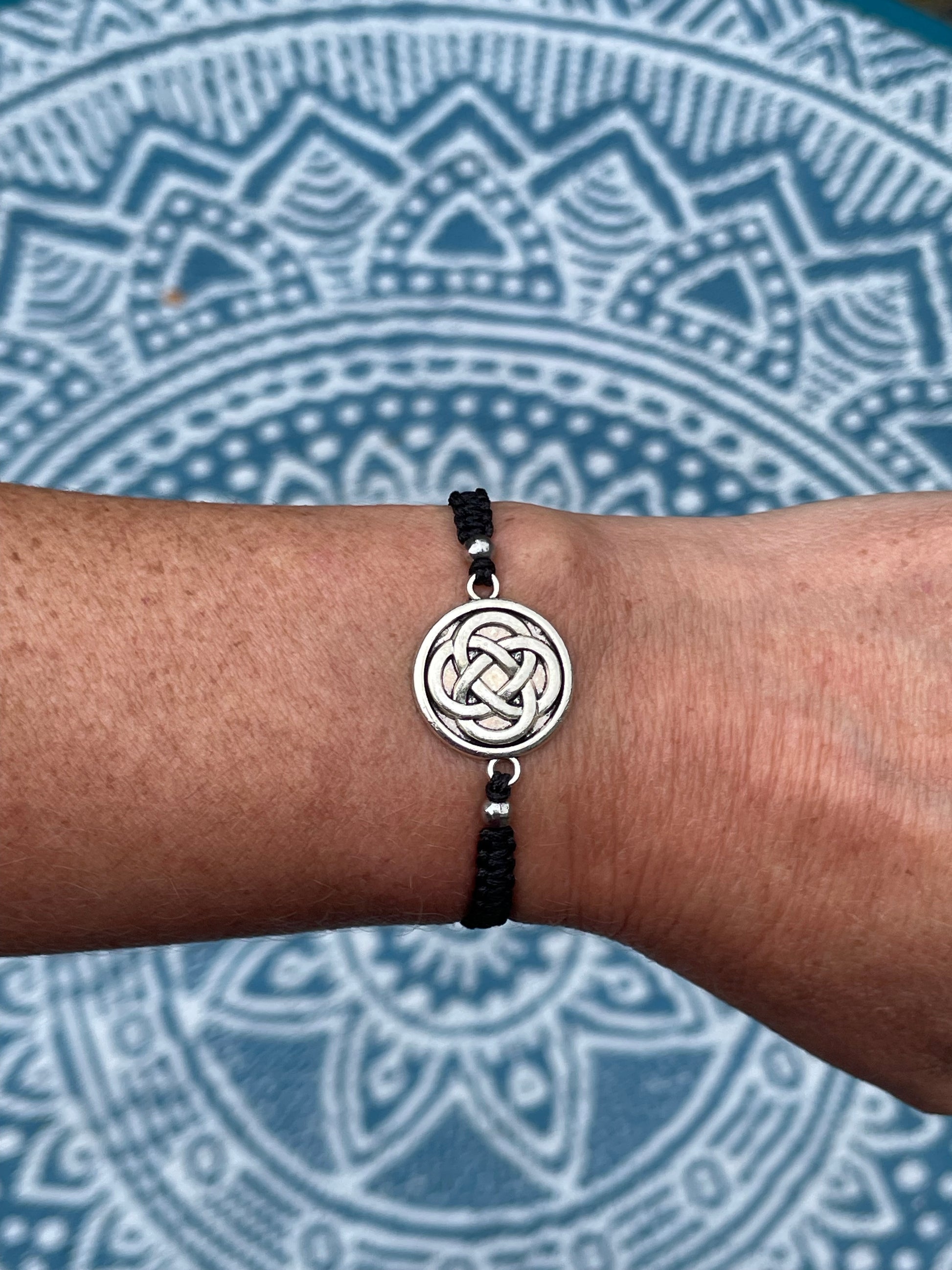 Celtic knot charm on macrame bracelet band with bead stoppers on wrist with mandala background