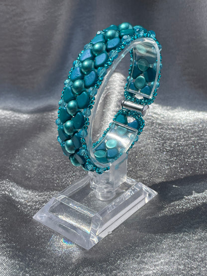 Teal coloured ginko bracelet on clear plastic stand with grey silk background