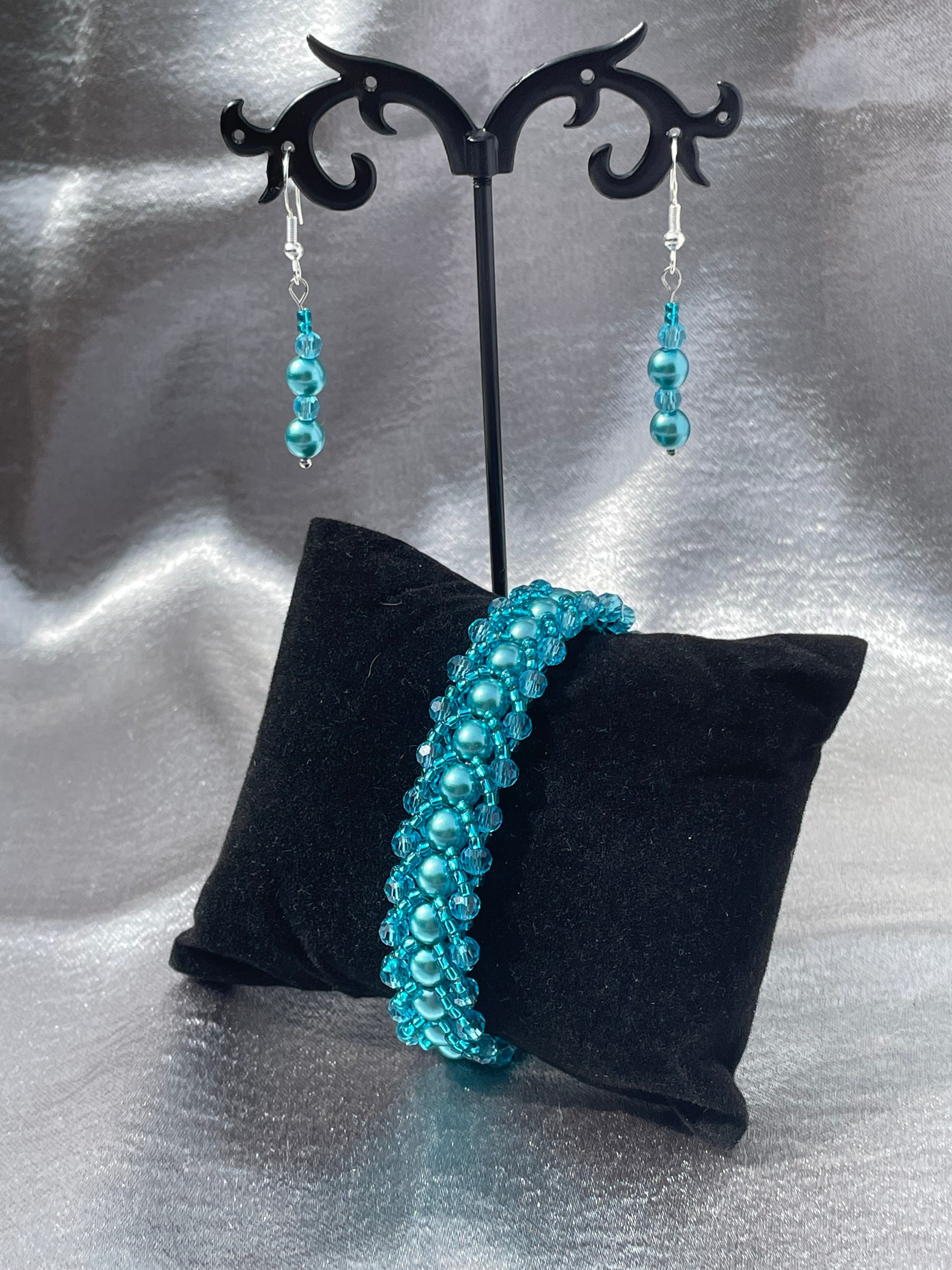 Crystal and pearl teal drop earrings with matching bracelet on black displays with silver satin background