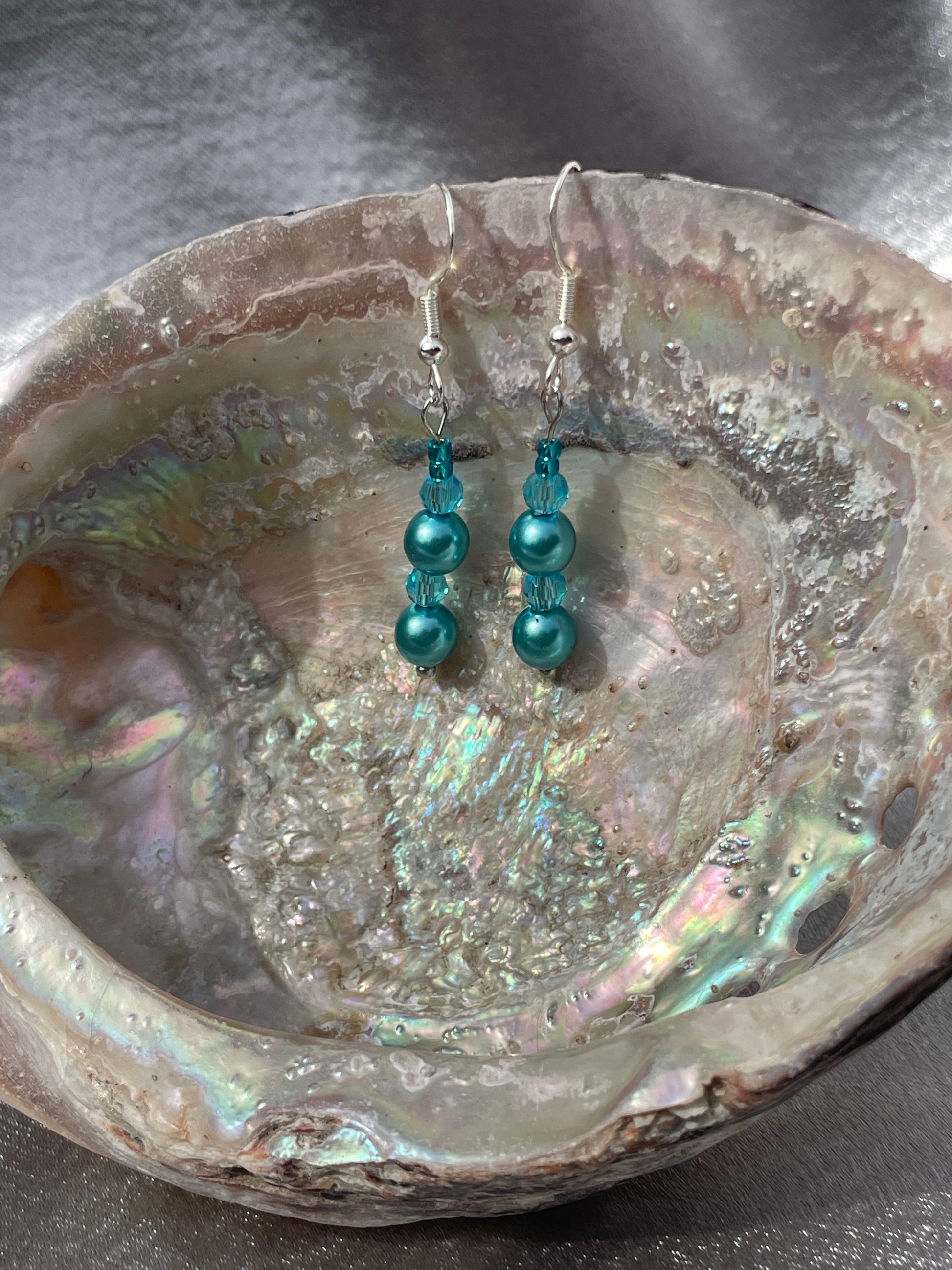 Crystal and pearl teal drop earrings sitting in abalone shell