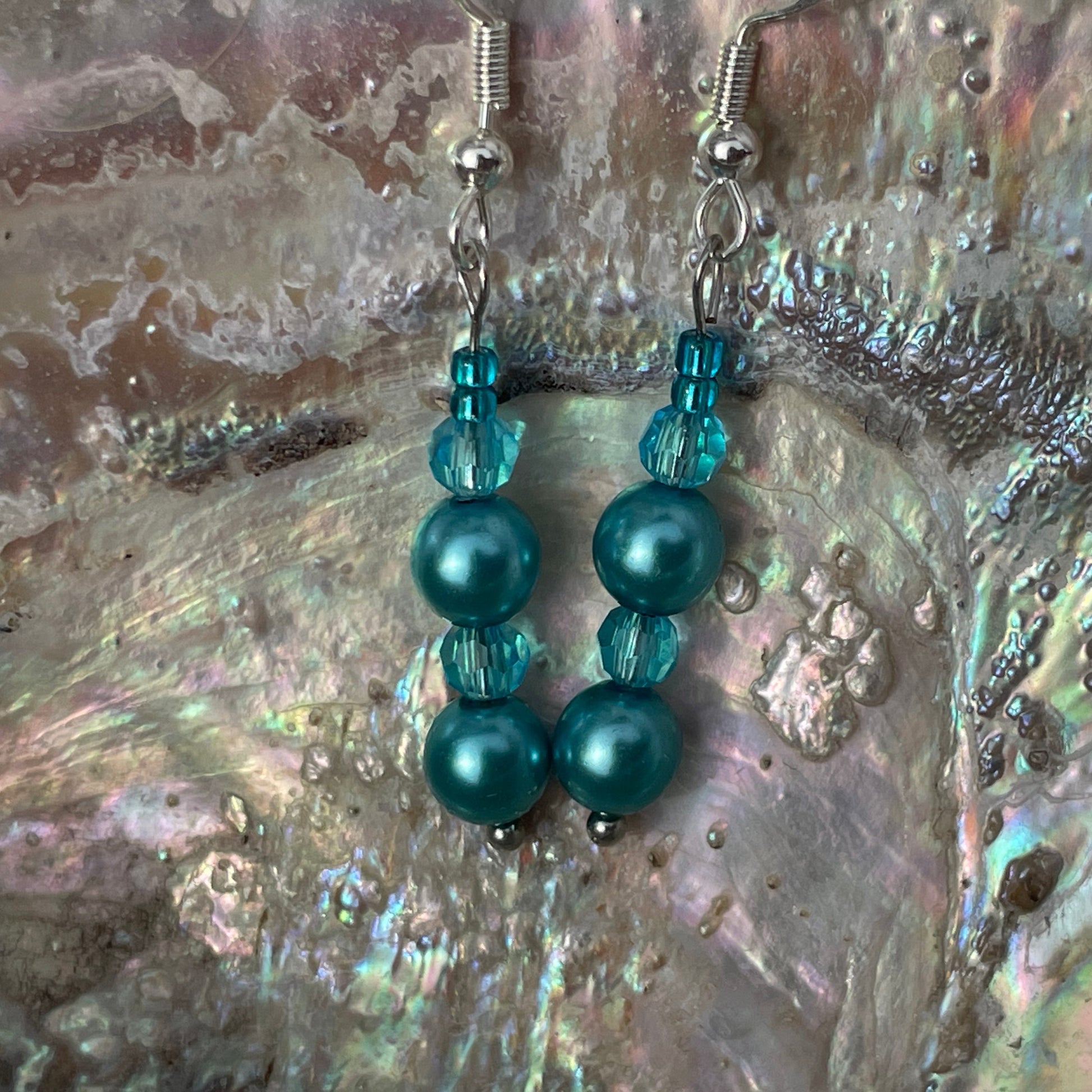 Crystal and pearl teal drop earrings close up with abalone shell background