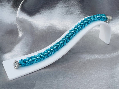 Teal pearl and crystal bracelet on white plastic stand with silver satin background