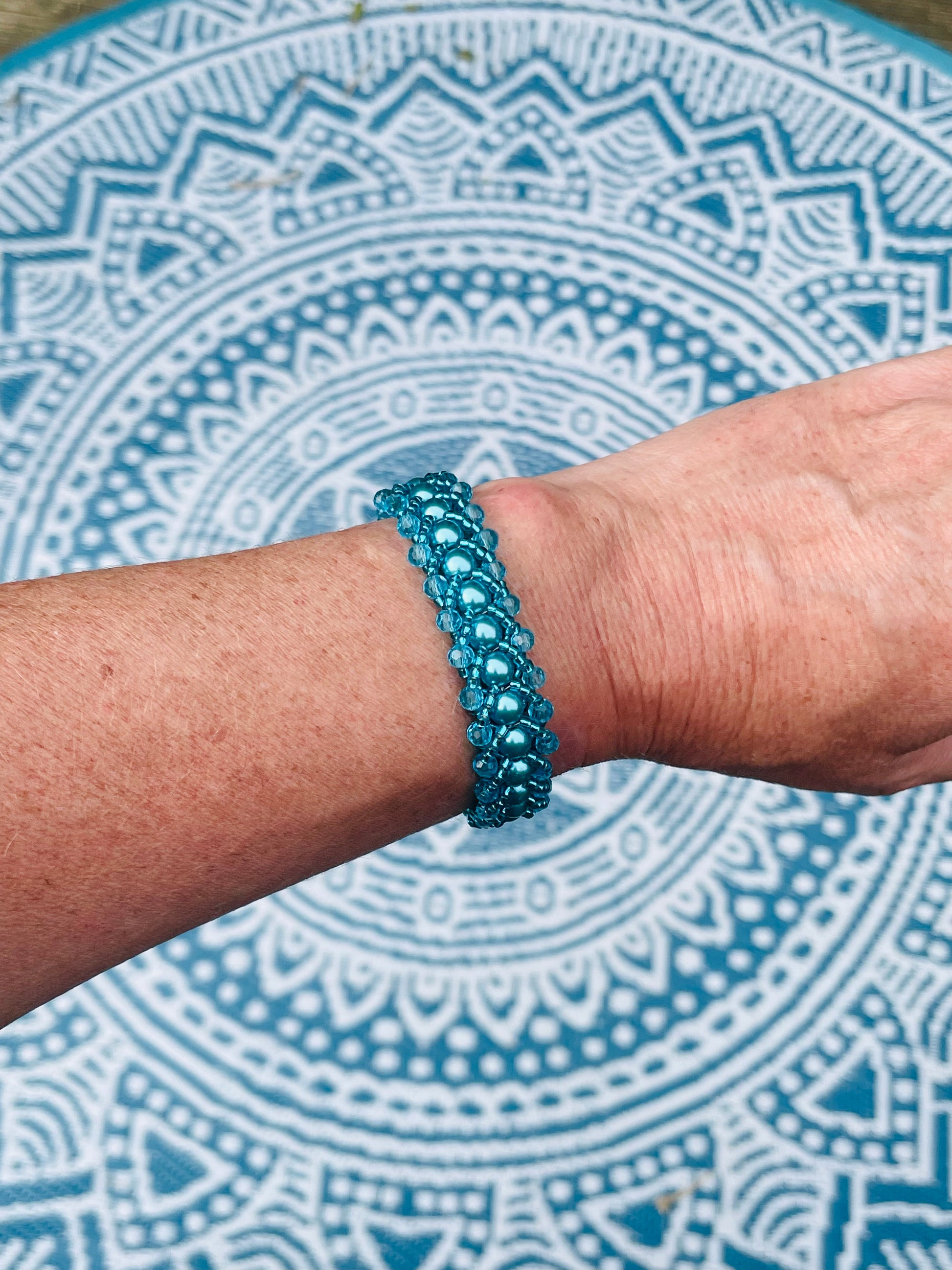 Teal pearl and crystal bracelet worn on wrist with mandala background