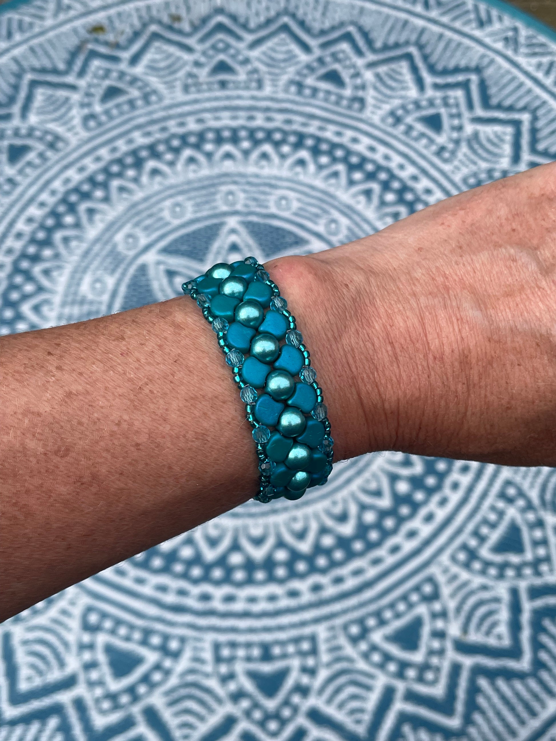 Teal coloured ginko bracelet worn on wrist with mandala pattern background