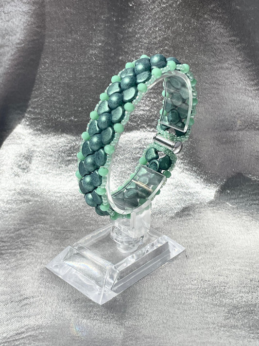 Green Czech glass and crystal bead bracelet on clear stand with silver satin background