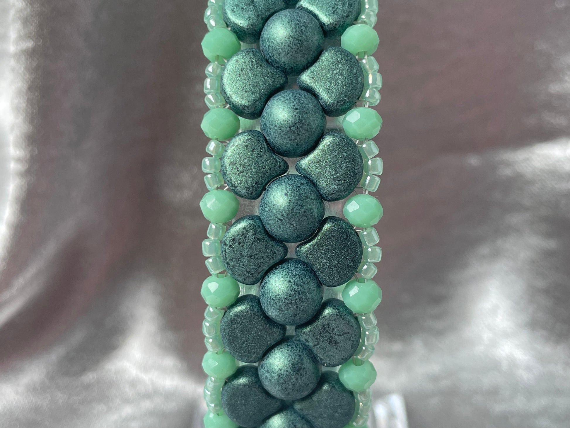 Close up of Green Czech glass and crystal bead bracelet on clear stand with silver satin background