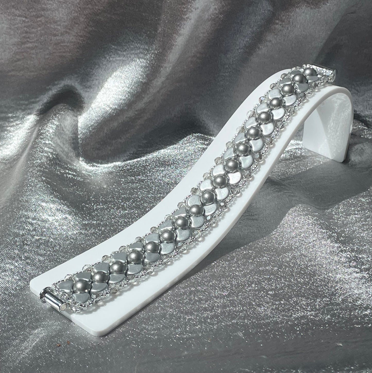 Silver Czech glass and crystal bead bracelet on a white plastic stand with silver satin background