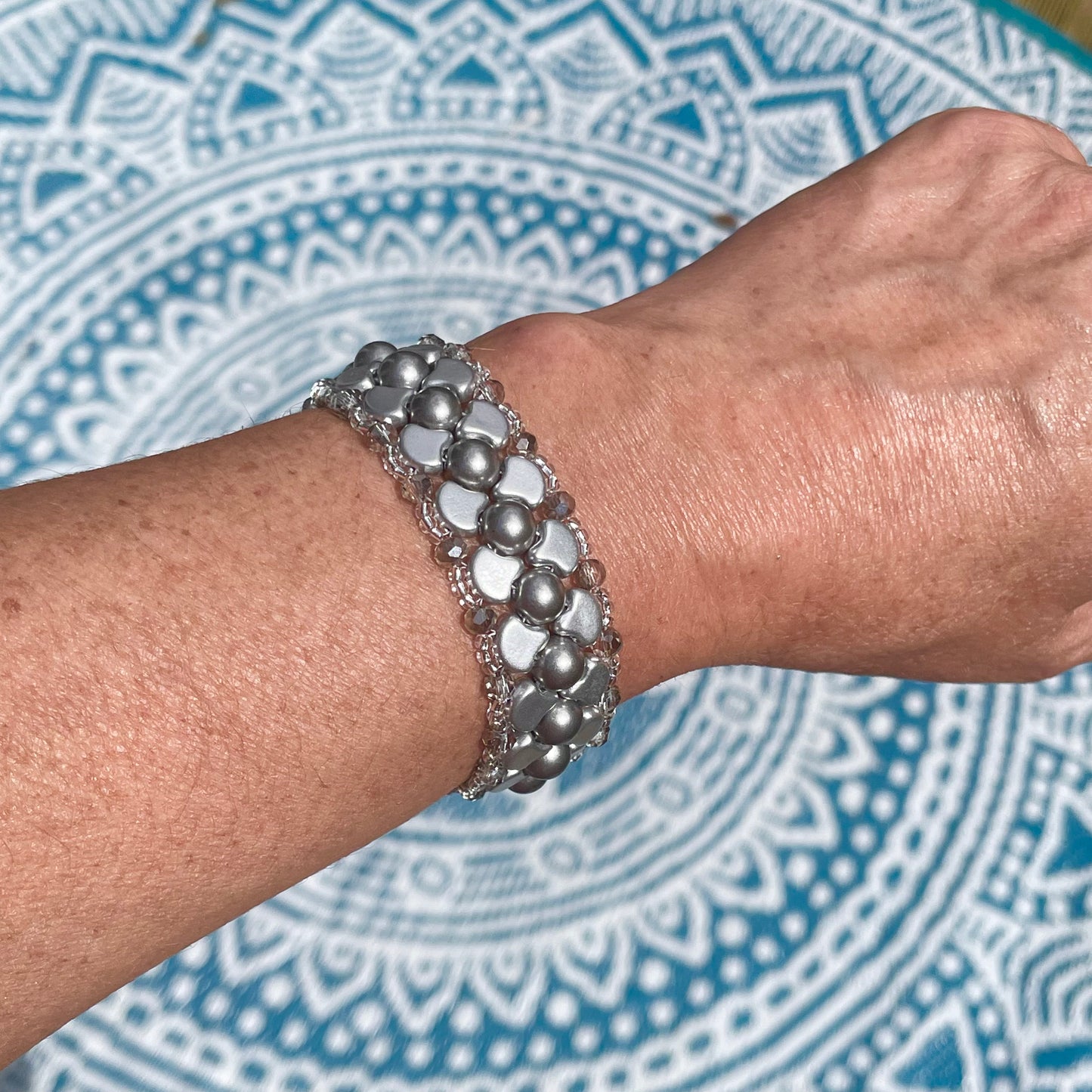 Silver Czech glass and crystal bead bracelet on a wrist with teal mandala background