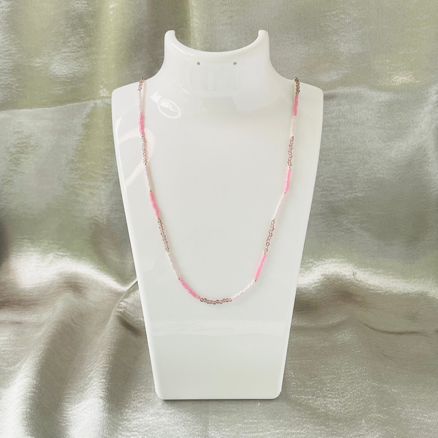 Seed bead and crystal necklace on white stand with silver background