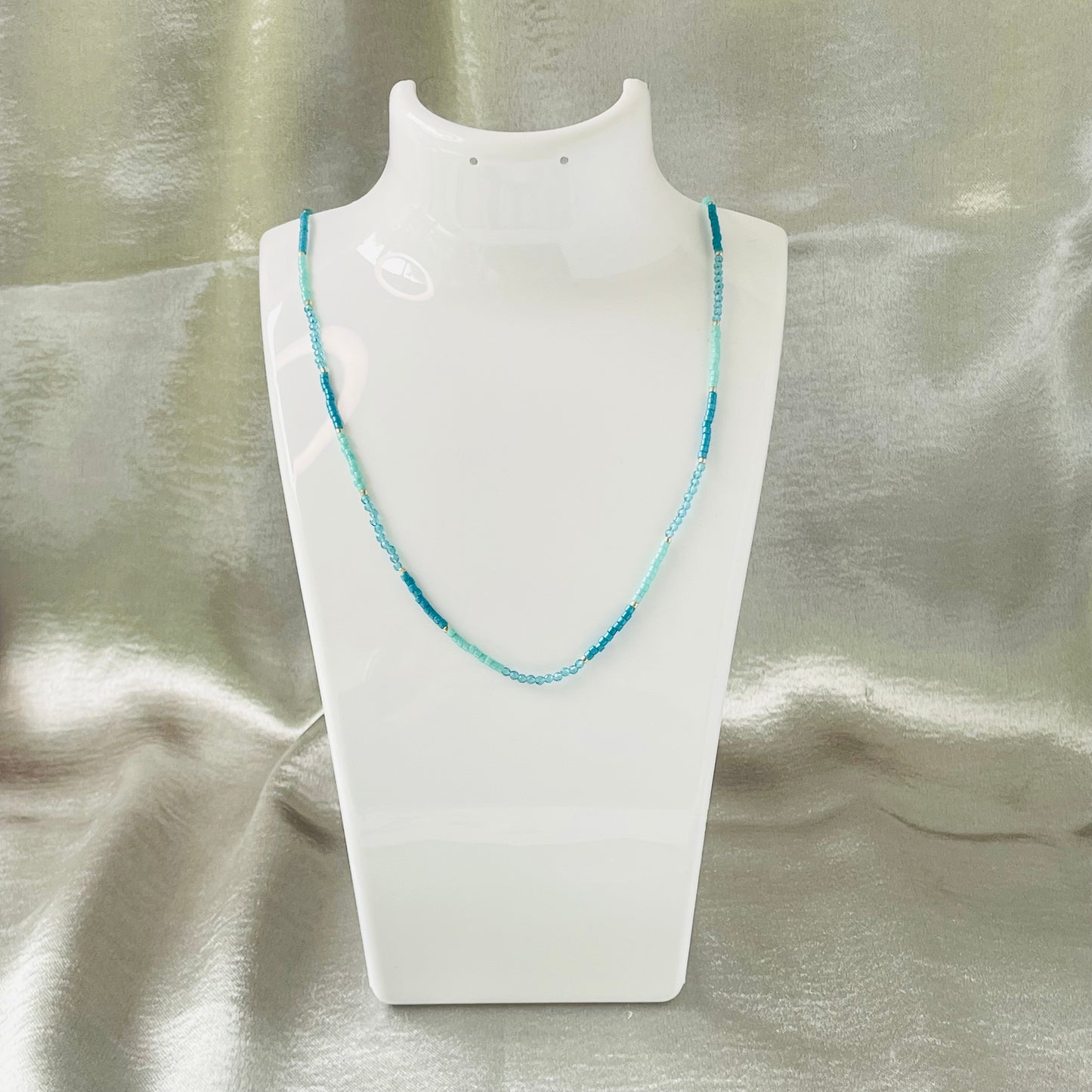 Seed bead and crystal necklace on white stand with silver background