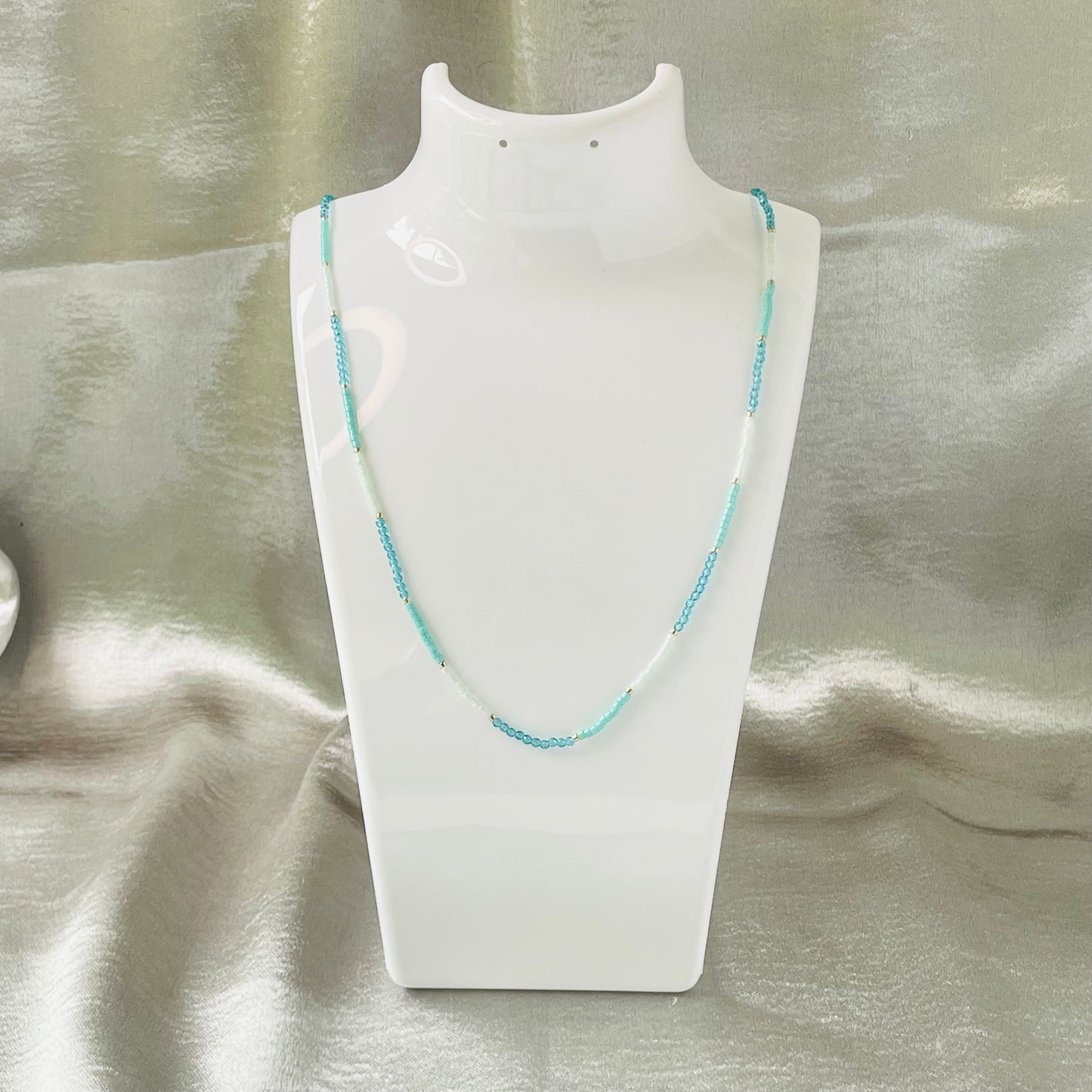 Seed bead and crystal necklace on white stand with silver background