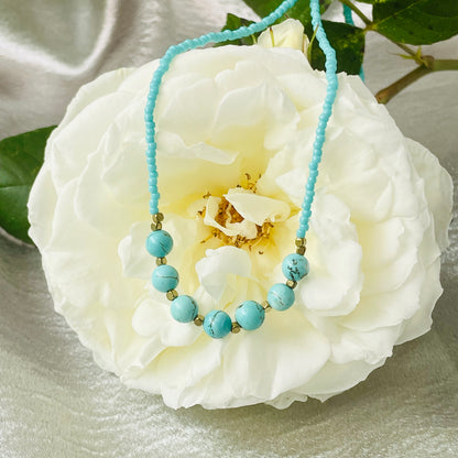 Turquoise seed and natural stone bead necklace with brass spacer beads on a white rose