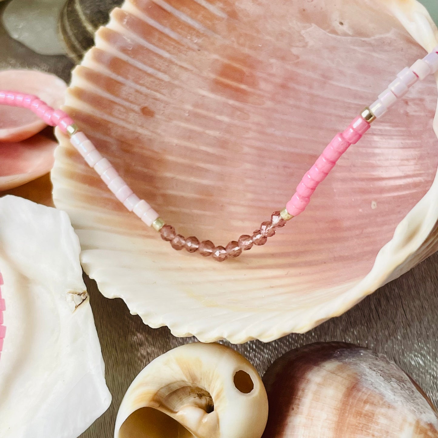 Close uop of seed bead and crystal necklace draped over seashells with silver background