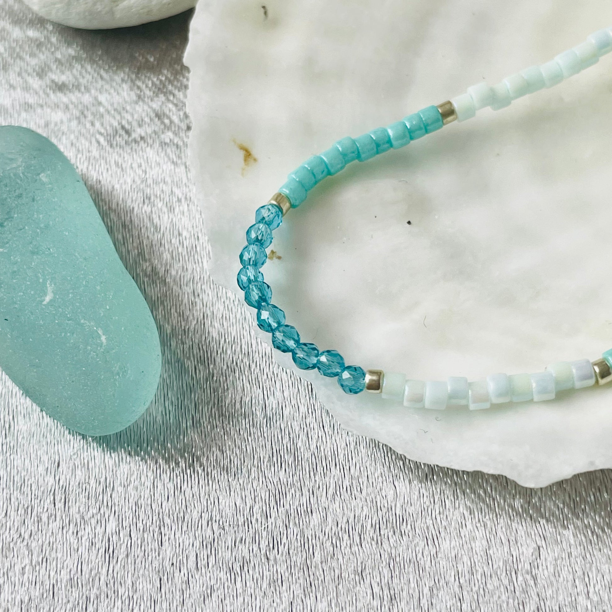 Close up of seed bead and crystal necklace on white shell with silver background