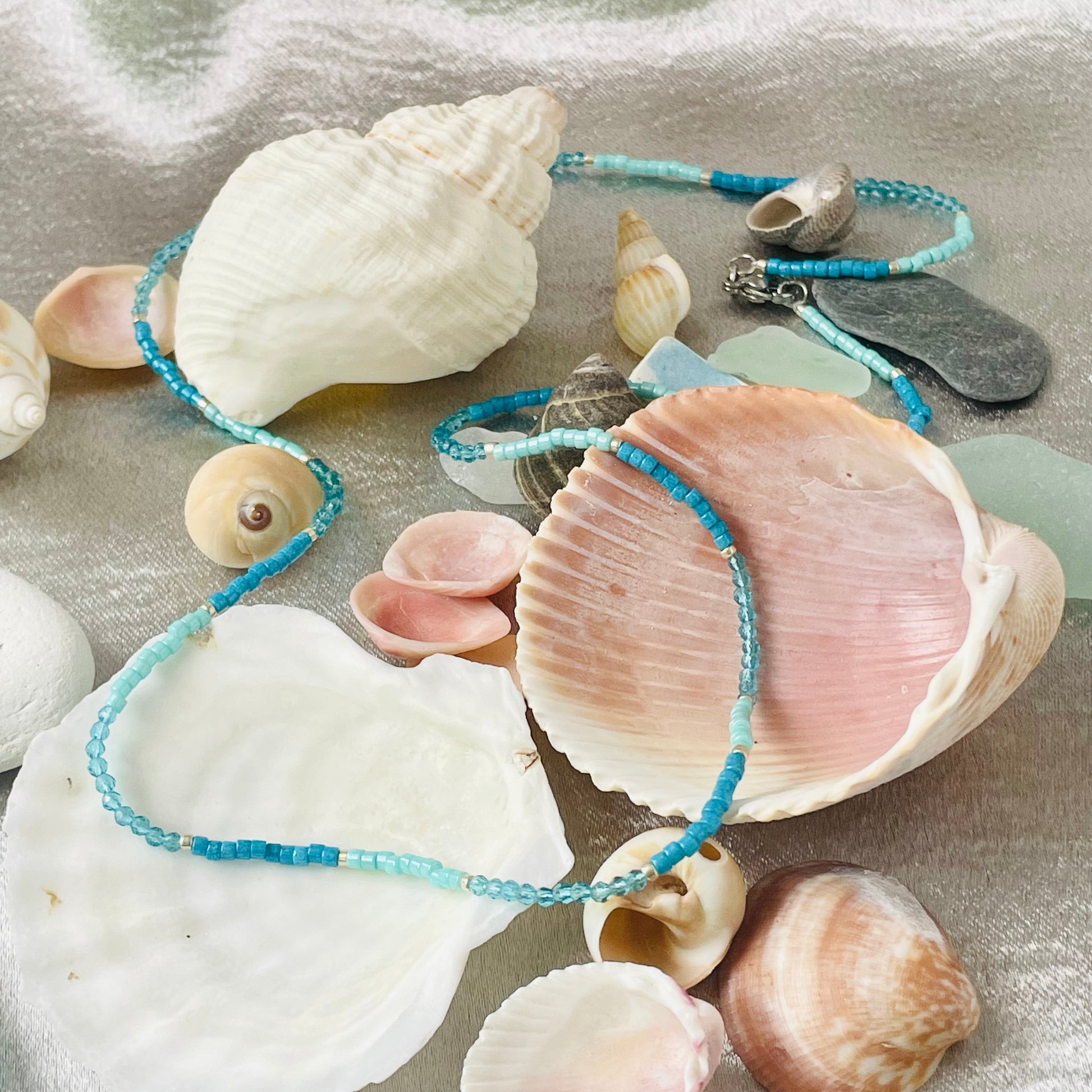 Seed bead and crystal necklace draped over seashells with silver background