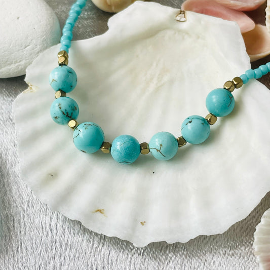 Turquoise seed and natural stone bead necklace with brass spacer beads on a white shell