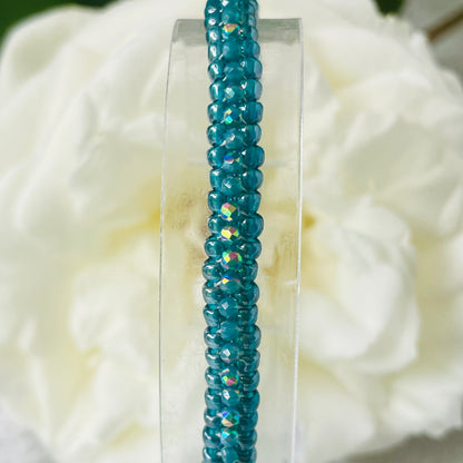 Close up of seed bead and crystal bracelet on clear stand with white rose in background