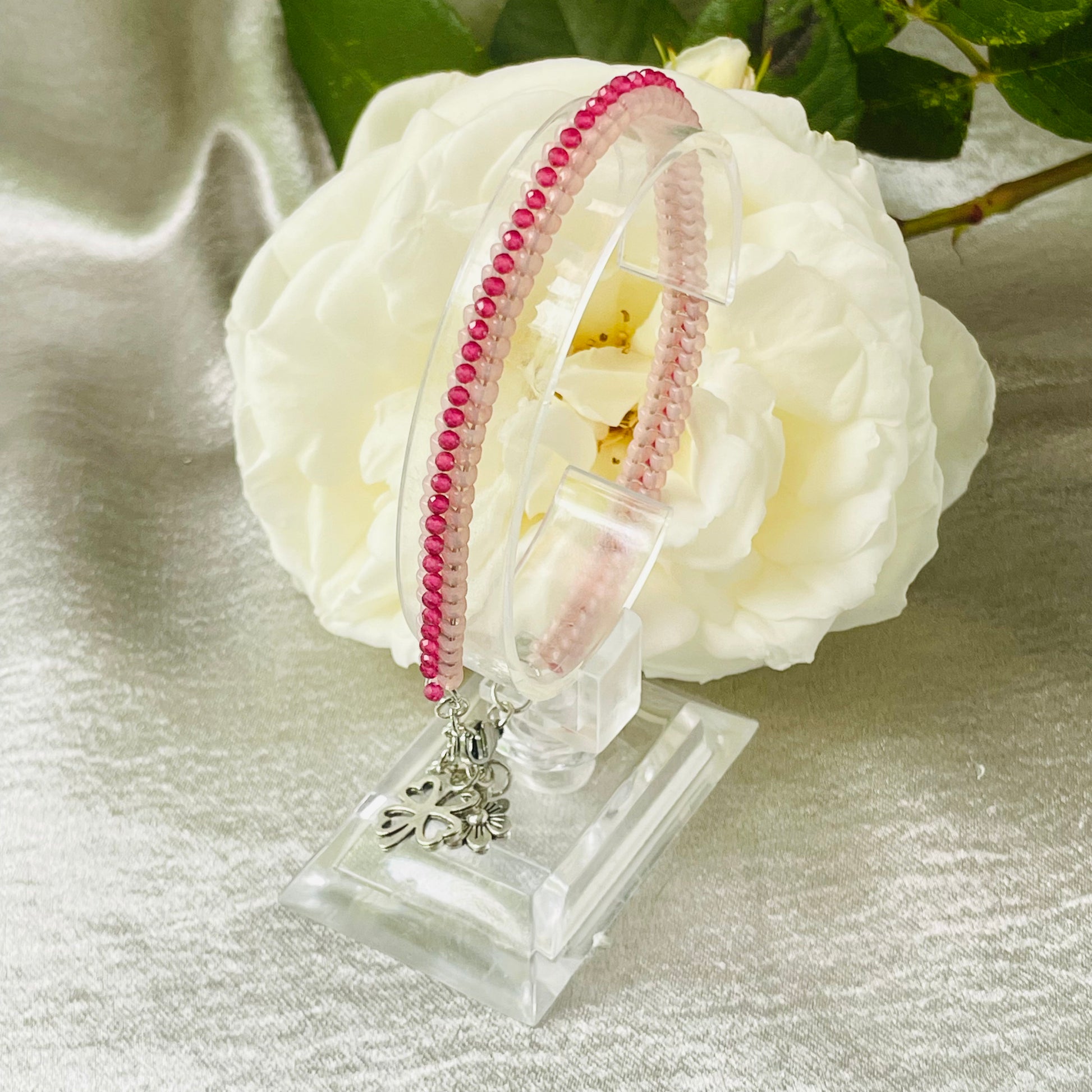 Seed bead and crystal bracelet on clear stand with white rose in background