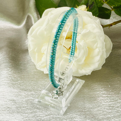 Seed bead and crystal bracelet on clear stand in front of white rose