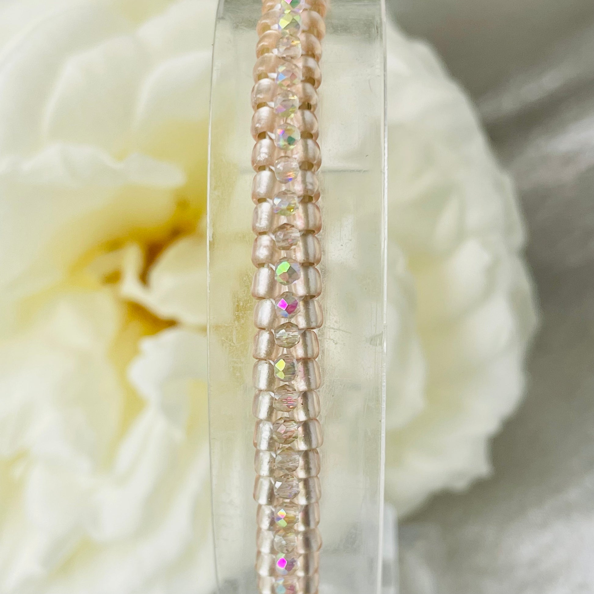 Close up ofSeed bead and crystal bracelet on clear stand with white rose in background